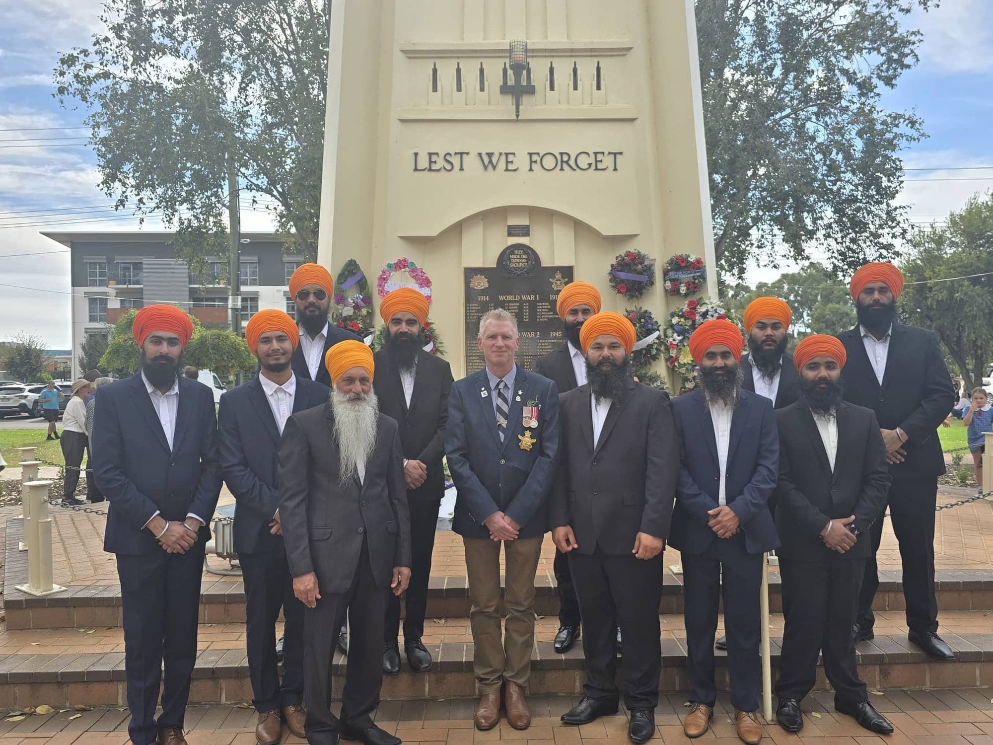 AKA members standing in front of a war memorial inscribed 'Lest We Forget'